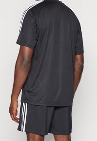 Černé sportovní tričko a šortky vyrobené z prodyšné tkaniny, s bílými pruhy po stranách a designem s kulatým výstřihem.