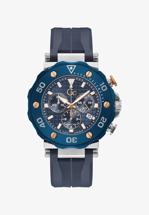 Sinine kroonograafi kell tekstureeritud dialiga, roosa kuldsete aktsentidega, roostevabast terasest kuppel ja sinine kummirihm. Veekindel kuni 100m.