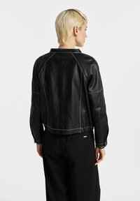 Czarna skórzana kurtka z białymi detalami, skrócony krój i rękawy raglanowe. Tył ma gładkie wykończenie i dopasowaną talię.