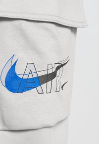 Svetlošedá tkanina s grafickým dizajnom, na ktorom sa v tučných, obrysových písmenách nachádza nápis "AIR". Akcenty zahŕňajú modrý prášok a susediacu čiernu zakrivenú čiaru.