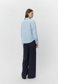 Helles blaues Langarmhemd mit gerafften Manschetten, Kragen und einer lässigen Passform, kombiniert mit navyblauen Weitbein-Hosen. Schlichte, minimalistische Gestaltung.