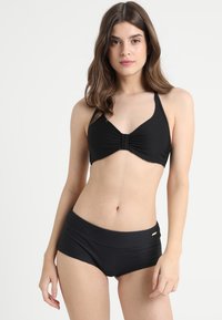 Zwart geribbeld bikini-top met een twistdetail in het midden en verstelbare halterbandjes; bijpassende zwarte high-waisted broek met platte naden.