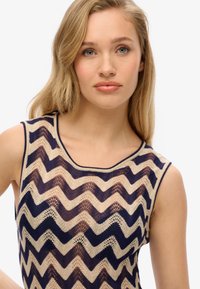 Gebreide mouwloze top met een zigzagpatroon in marineblauw en beige, voorzien van een open geweven textuur en een ronde halslijn.