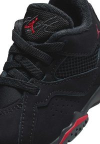 Baskets noires en matériaux mesh et daim, avec des accents rouges, des détails perforés et des lacets noirs. Col texturé pour le confort.