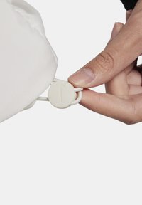 Una bolsa de tela blanca con cordón sostenida por una mano, que presenta un cierre redondo beige con el logo de Nike. La bolsa tiene una textura suave.