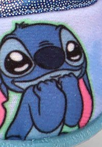 Personaje de dibujos animados azul con grandes ojos y patas cerca de su cara, mostrando una expresión tímida o nerviosa sobre una superficie de tela.