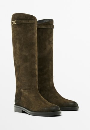 Bottes jusqu'aux genoux en daim marron foncé. Bout arrondi, semelle en caoutchouc plate, et accent doré en haut. Texture lisse avec un minimum de détails.