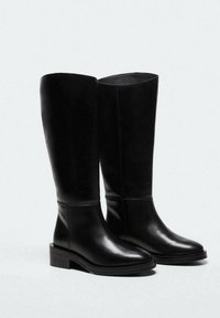 Bottes montantes en cuir noir avec une finition lisse, bout rond, petit talon bloc et design minimaliste. Silhouette épurée et structurée.