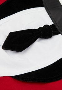 Pajarita de terciopelo negro sobre un fondo de tela blanca, con textura suave y un borde negro brillante, colocada sobre una superficie roja.