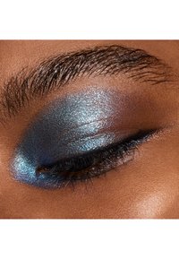 Close-up of an eye with vibrant blue and silver shimmer eyeshadow, finely textured, contrasting against smooth, dark skin and prominent eyelashes.