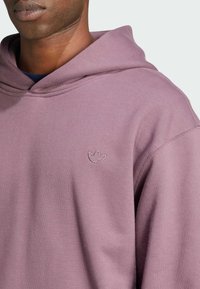 Pullover hoodie i dämpad lavendelfärg, med en kenguruficka, ribbade ärmslut och en liten broderad logotyp på bröstet.