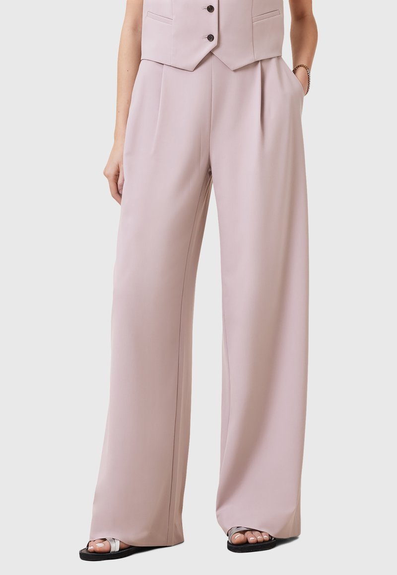 Lichtroze wijde broek van gladde stof, met plooien en zijzakken. Draag met een vest en casual zwarte sandalen.