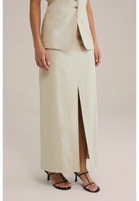 Beige linnen maxi rok met een split aan de voorkant, rechte vorm en schone naden. Gecombineerd met zwarte sandalen met bandjes. Formeel ontwerp geschikt voor evenementen.