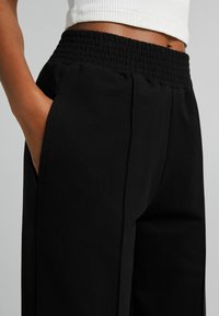 Svarta byxor med en rynkad elastisk midja, sidofickor, raka ben och en mjuk, lätt tygkvalitet.