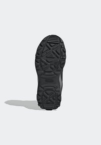 Semelle extérieure de chaussure de sport noire avec un motif de grip texturé et des crampons triangulaires distinctifs, arborant le logo "Traxion" pour une meilleure adhérence.