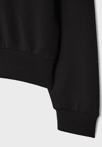 Sweat-shirt noir à manches longues avec poignets et ceinture côtelés présenté sur un fond gris clair.