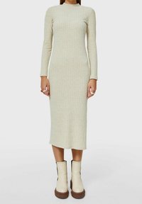 Robe midi en maille beige clair avec texture côtelée. Manches longues et encolure ronde. Portée avec des bottines blanches épaisses avec des accents noirs.