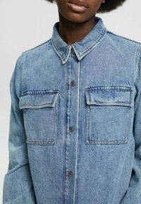 Ljusblå denimskjorta med knäppning fram, två bröstfickor och klassisk krage. Strukturerad tyg med synlig sömnad.