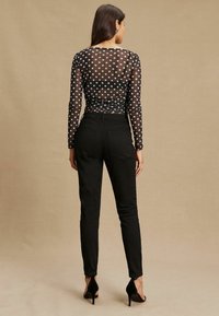 Permatomas juodas ilgomis rankovėmis viršus su baltomis taškuotomis dėmėmis, derinamas su juodomis aukšto liemens kelnėmis ir juodais stiletto aukštakulniais. Neutralus fonas.