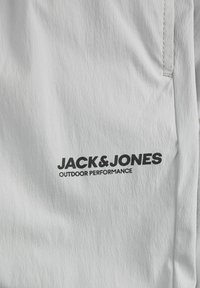 Hvidt stof med en tekstureret overflade, der har et sort logo, som viser "JACK & JONES" med "OUTDOOR PERFORMANCE" nedenunder.