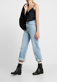 Schwarzes Satin-Camisole mit Spitzenbesatz, hellblaue Jeans aus Denim mit aufgerollten Säumen und schwarze Ankle-Boots mit Blockabsatz.