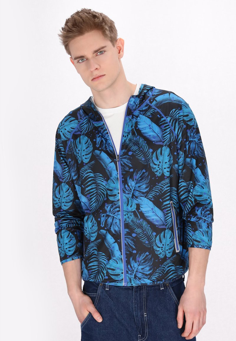 Hooded jack met een blauw tropisch bladpatroon op een zwarte achtergrond. Voorzien van een ritssluiting aan de voorkant en 3/4 mouwen. Gemaakt van lichte stof.