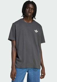 Tmavo sivé bavlnené tričko s okrúhlym výstrihom a krátkymi rukávmi, s bielym logom troch pruhov v tvare listu konope na ľavej strane hrudníka.