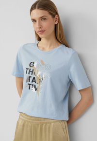 Lichtblauwe katoenen T-shirt met korte mouwen, ronde halslijn, met een gedrukt grafisch ontwerp in zwart, zilver en beige tekst en accenten.