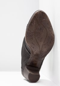 Semelle en cuir marron usée d'une chaussure à talon noire texturée reposant sur une surface d'angle blanche.