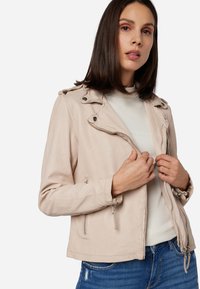 Ljusbeige imitation läderjacka med dragkedja framtill, knappad krage och fickor med dragkedja. Har en figurnära design och slät yta.