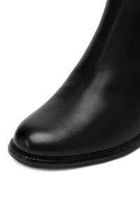 Botín de cuero negro conpuntera afilada, textura suave y una costura a lo largo del borde de la suela.