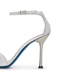 Sandalo bianco con tacco alto e cinturino alla caviglia, finitura lucida in patinato, dettagli metallici e interno blu. Tacco a stiletto sottile e punta affilata.