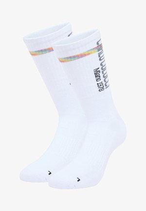 Hvide bomuldsokker med ribbet tekstur, der har en farverig stribe øverst og trykt tekst i sort på den ydre side.