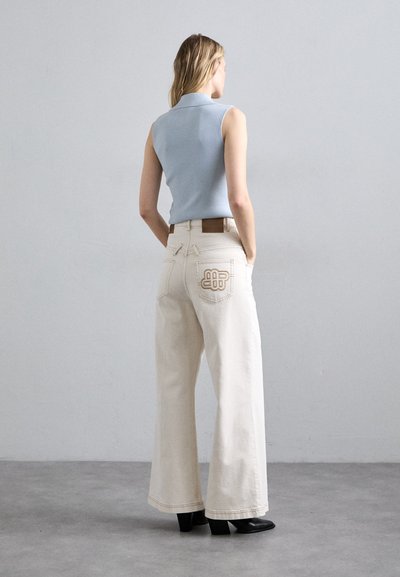 Jasnoniebieski bezrękawnik o prążkowanej strukturze w zestawieniu z beżowymi dżinsami o szerokich nogawkach z haftowanymi tylnymi kieszeniami oraz brązowym paskiem. Czarne botki za kostkę.