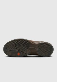 Suela de un zapato marrón con patrones de huella ondulados y un detalle circular naranja cerca de la bola del pie sobre un fondo gris.