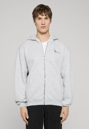 Pilkas zip-up sportinis džemperis, pagamintas iš minkštos medžiagos, su reguliuojamu kapišonu, priekinėmis kišenėmis, raukinėtais rankogaliais ir subtiliu logotipu kairėje krūtinės pusėje.