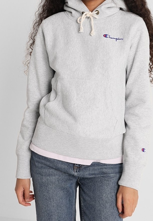 Gray fleece hoodie with a drawstring hood, front pocket, and embroidered logo. Worn over a light pink shirt, paired with blue jeans.