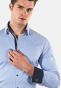 Camicia a quadri blu con colletto button-down, polsini neri a contrasto e design aderente. Tessuto liscio con un aspetto strutturato.