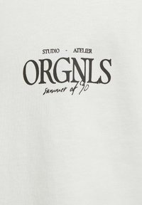 Hvid bomulds t-shirt med sort trykt tekst: "STUDIO - ATELIER ORGNLS sommeren '90." Glat tekstur, enkel typografi.