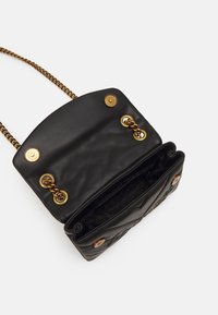 Czarna pikowana skórzana torebka na ramię z złotym łańcuszkiem, otwarta klapa pokazująca wnętrze wyłożone materiałem oraz złote zapięcia na zatrzask.
