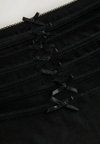 Six black fabric edges with stitched trim and small black satin bows aligned diagonally on a dark background.