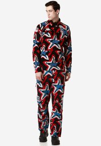 Giacca e pantaloni a motivi rossi, blu e bianchi con forme a stella, dotati di mezza zip e loghi. Il materiale sembra morbido e strutturato.