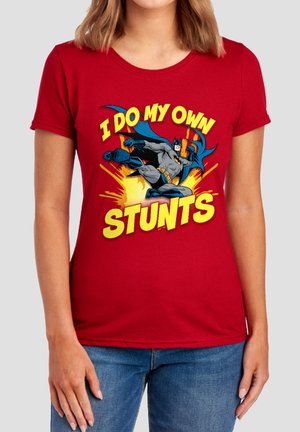 Woman wearing a red t-shirt with Batman kicking and text saying "I do my own stunts" in bold yellow letters.