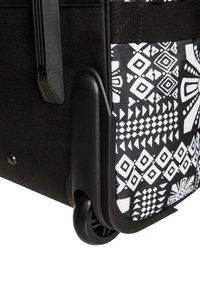 Czarna walizka na kółkach z białym geometrycznym wzorem, wykonana z trwałego materiału, z wzmocnionymi narożnikami i solidnymi gumowymi kółkami.