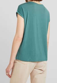 Teal kortärmad t-shirt med avslappnad passform och rullade ärmar. Mjuk tyg, rund halsringning och rak fåll. Bärs med ljusbeiga byxor.