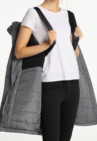 Šedá vnější bunda s nadýchanou šedou vnitřní podšívkou. Má zipové zapínání, boční kapsy a černé ramenní popruhy.