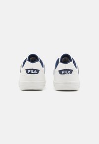 Sneakers bianchi con dettagli blu navy e materiale testurizzato sulla linguetta. Presentano un logo Fila ben visibile sul tallone. Suola in gomma piatta.