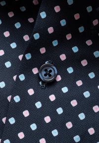 Mustast kangast, millel on vahelduvad read väikeste roosade ja siniste ümarate ruudukujuliste mustritega ning keskel õmmeldud must neljakanaline nööp.