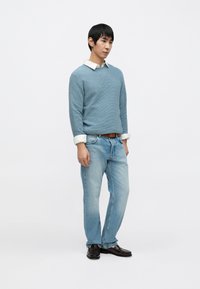 Svetlomodrý textúrovaný sveter cez bielu košeľu s golierom, v kombinácii so svetlomodrými džínsami a tmavohnedými topánkami. Jednoduchý dizajn, ležérny strih.