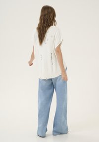 Weißer, oversized gestrickter Pullover mit sichtbaren Nähten, kombiniert mit hellblauen, weit geschnittenen Jeans. Lässiges Design mit lockerer Passform.